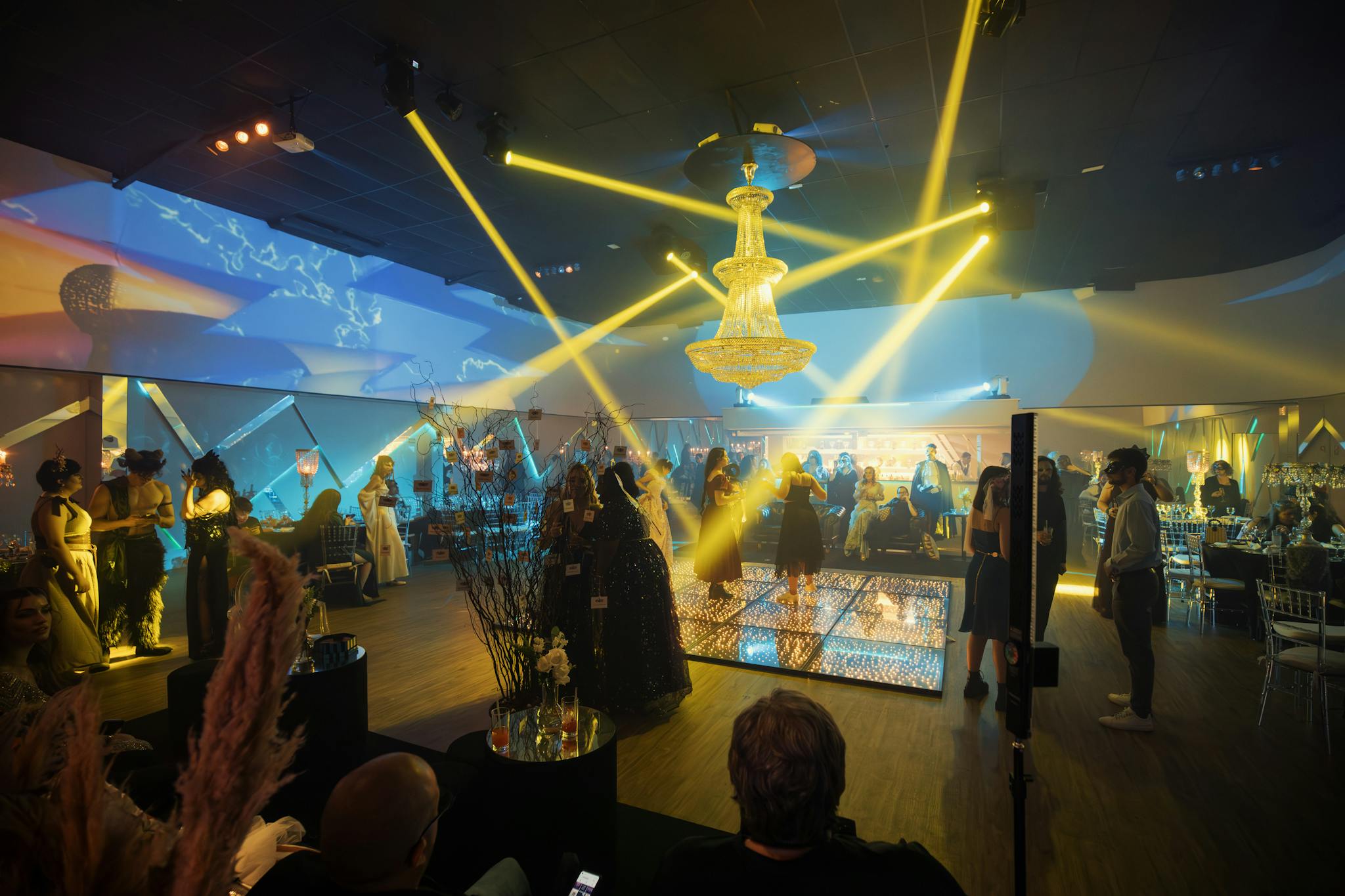 A stylish party scene with guests and a dance floor under dramatic lighting.
